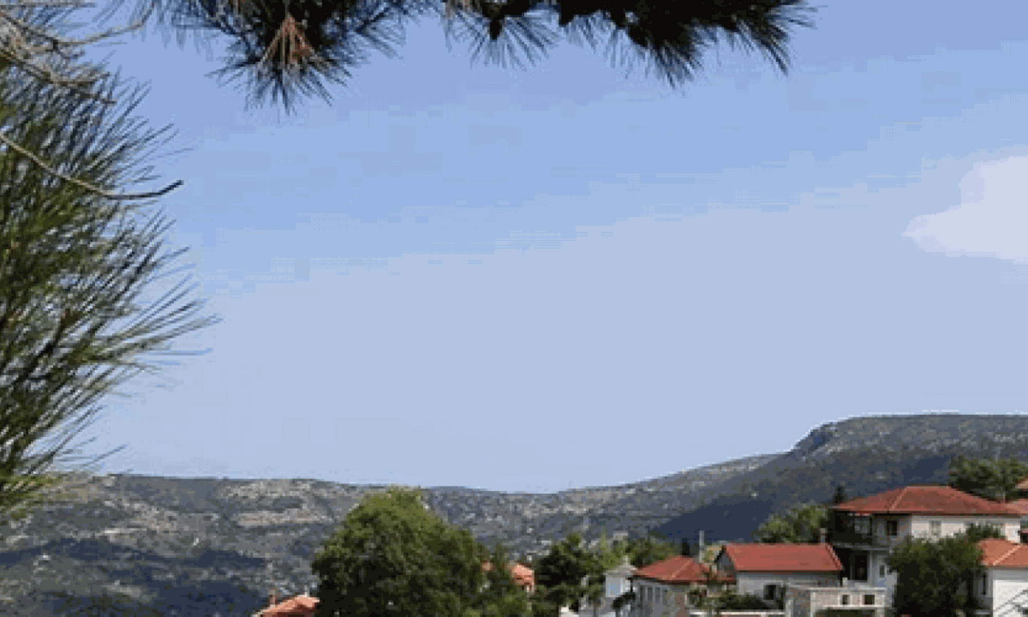 Hillside village with red-tiled roofs framed by pine branches and mountains
